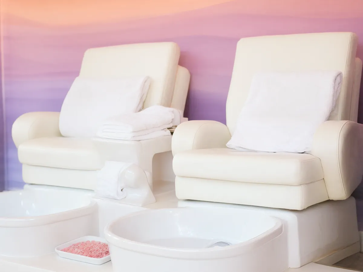 Two white pedicure chairs in front of a wall painted in bands from peach to lilac