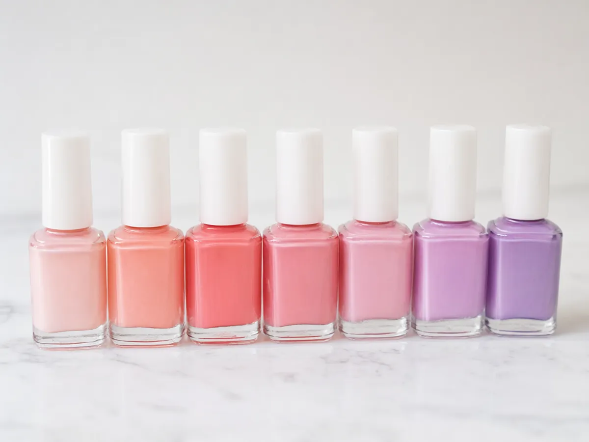Nine nail polish bottles in a row shading from blush pink to coral to lilac
